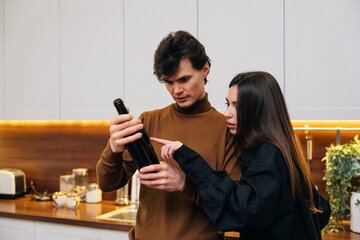 Couple examines wine bottle in modern kitchen during evening gathering