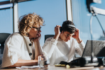Two business employees engaged in focused work at a bright, modern office. They are deeply immersed...