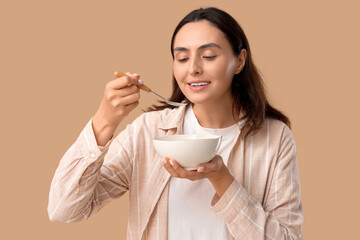 Young woman eating tasty soup on beige background