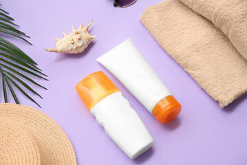 Composition with bottles of sun cream, towel, hat and palm leaf on lilac background