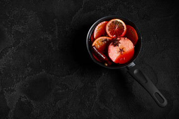 Saucepan of hot mulled wine with apple and different spices on black background