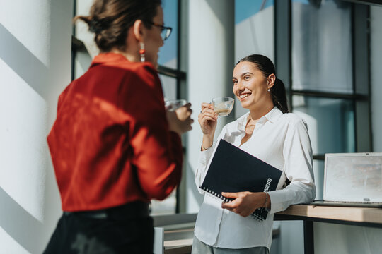 Business colleagues share a conversation while enjoying coffee in a bright office setting. The atmosphere is relaxed and professional, capturing a moment of casual interaction during a workday break.