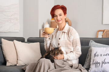 Obraz premium Beautiful happy mature woman with cute cat and cup of tea sitting on sofa at home