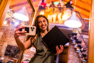 Young woman taking a celebratory selfie holding her graduation cap during a joyful party with...