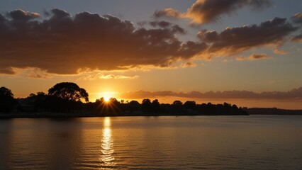 Naklejka premium Sunset over calm water with silhouetted trees.
