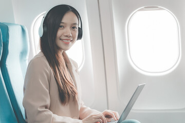 Fototapeta premium Travel of an Asian business woman working using a laptop computer. A successful Asian woman in an airplane cabin during a flight.