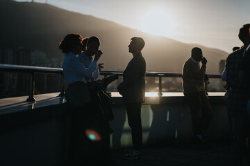 A diverse group of business colleagues brainstorm on a high tower balcony as the sun sets, showcasing a multicultural collaborative atmosphere. - Powered by Adobe