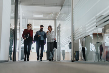 Fototapeta premium A group of colleagues walk down a bright corridor in a contemporary office, engaged in conversation and teamwork. The scene captures a dynamic and collaborative business environment.