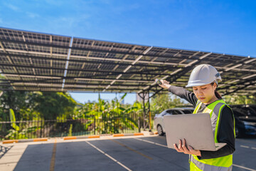 Fototapeta premium Engineer inspecting a solar powered carport with a laptop, highlighting the integration of renewable energy in modern infrastructure. Solar panels provide shade for parked vehicles in an eco-friendly 