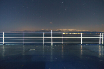 View from deck of car ferry boat to the coast with snow covered mountain peaks in moonlight and stars on the night sky, Greece