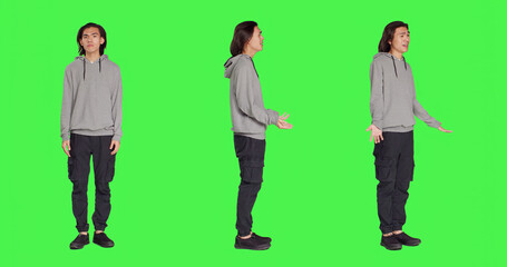 Obraz premium Young unsure guy shrugging on camera, doing i dont know sign after hearing question. Model feeling clueless and uncertain over full body greenscreen backdropground, doubtful person.