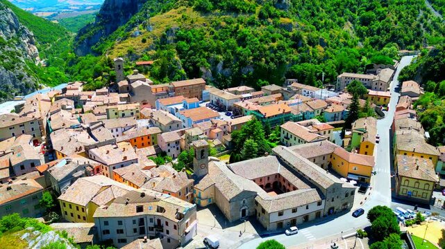 Superb aerial pedestal up shot from the Pioraco's town center, road with passing cars, closely knit buildings with pastel colors, belltower, surrounded by impressive Sibillini mountains and a gorge