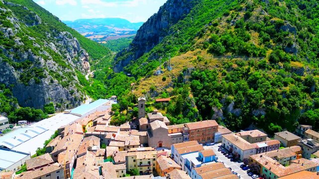 Fantastic aerial pullback pedestral up shot from Pioraco, visuals starting from the town square and belltower, widening with manifold civil and industrial buildings, near the majestic Sibillini gorge