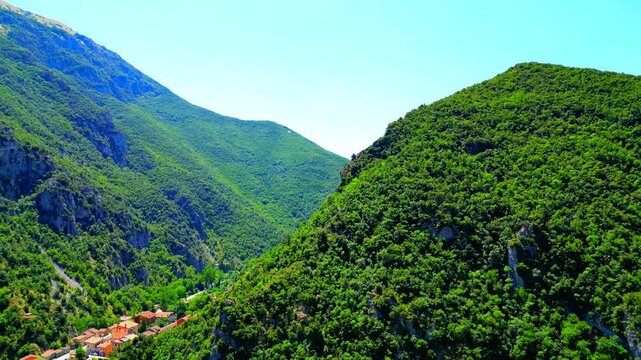 Majestic aerial pan left shot of the Sibillini Mountains as seen from Pioraco, an overview of their minutely green-topped crests with rocky stumps surrounding a deep gorge with human settlements