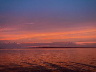 Fototapeta premium purple and orange sunset with clouds over the water on lake with waves