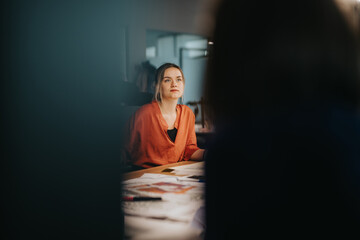 A focused businesswoman in an orange blouse engages in a meeting, discussing ideas and strategies...