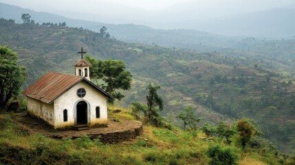 Fototapeta premium A quaint church on a hillside surrounded by lush green mountains under a cloudy sky.