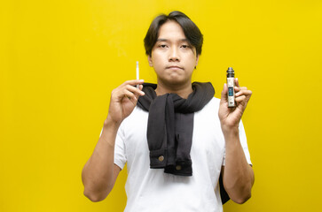 Fototapeta premium Cigarette vs E-Cigarette Concept. Young Asian Man Smoking and Vaping with Thick Smoke.