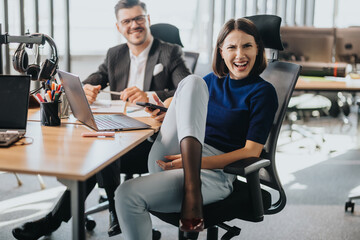 Fototapeta premium Multicultural business employees laughing and working together in a modern office setting, exhibiting teamwork and productivity. The scene conveys a positive and collaborative work environment.