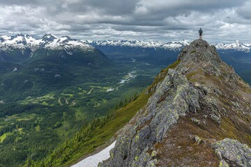 Fototapeta premium A hiker stands atop a rocky peak, overlooking a breathtaking mountainous landscape.
