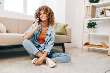 Happy woman holding a mobile phone on the cozy sofa at home, enjoying online games and chatting in...