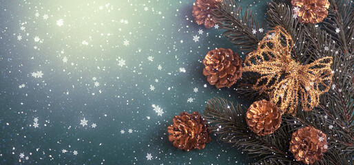 Christmas background with decorative fir tree branch, golden bow and cones for decoration. New Year winter holidays concept with decor in blue and gold colors and copy space, snowy top view banner.