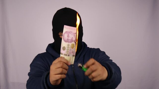 close up on the thief burning his ten thousand Singapore dollar banknotes and wearing a jacket with a white background.
