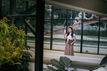 Young asian businesswoman holding a laptop under her arm and taking pictures with her phone in a...