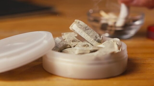 Snus nicotine tobacco close up, pack of tobacco for gum. unhealthy addiction. Man opening box with snus and taking one. 