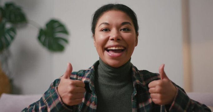 Excited Hispanic woman with toothy smile gives thumbs up