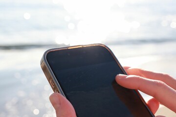 海が見える場所で、スマートフォンを操作する女性の手