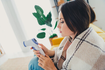 Young woman checking temperature with infrared thermometer at home during a relaxing day indoors