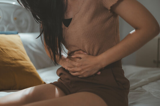 Close-up of woman feeling stomachache, nausea, bloating and cramps. Discomfortable menstruating woman sitting on bed with stomachache.