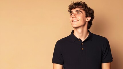 Fototapeta premium Cheerful young man with curly hair wearing dark polo shirt, smiling against beige background, exuding positive and confident vibe