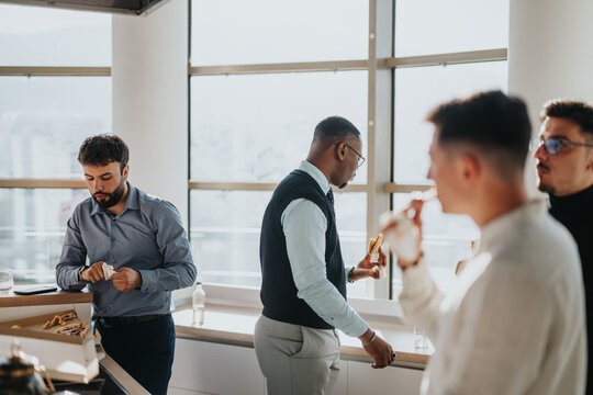 A diverse group of business people enjoy a relaxed break in a modern office setting, fostering teamwork and collaboration. They are seen eating snacks and engaging in light conversation.