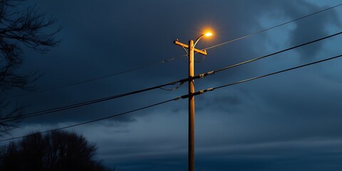 Landscape photograph featuring a wooden utility with wires and light on street, dark night with spart of utility lightbulb