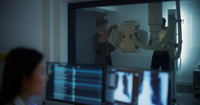 Male Nurse Assisting a Patient in Positioning Himself Before an Advanced X-ray Machine, Ensuring a Precise Procedure. Behind the Window, Female Radiologist Analyzing Body Scans on a Computer Monitor
