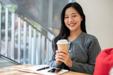 A beautiful woman sitting at a table in a cafe, holding a hot drink cup and smiling at the camera.