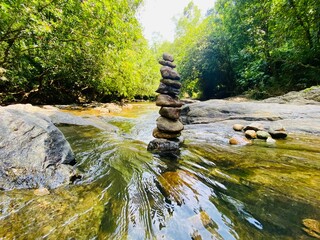 A serene scene of a stack of smooth rocks balanced atop a flowing river, symbolizing harmony,...