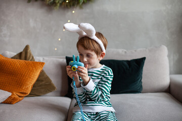 Little boy sitting on sofa and looking photos on his digital camera for kids. Child wearing striped...