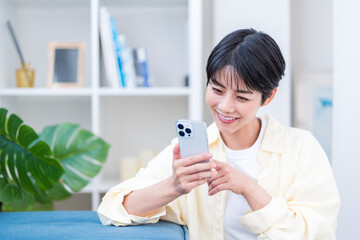 リビングででスマホを操作している若い女性。