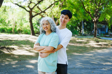 Obraz premium A happy senior mother embraces her smiling adult son in a lush green park. Surrounded by nature, their affectionate hug symbolizes love, peace, vitality, and renewal under the serene greenery