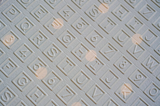 Close-up view of a textured surface with embossed alphabet and numbers. A repeating pattern in a gray color. Embossed Alphabet and Numbers Texture on Grey Surface.