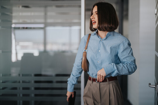 Professional businesswoman confidently enters a modern office environment, ready for a meeting. Her poised demeanor and stylish attire reflect preparation and determination in a corporate workplace