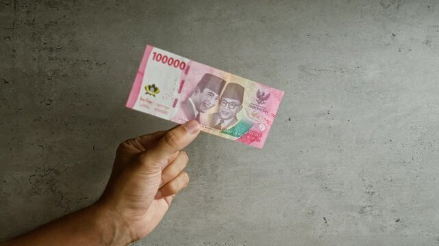 Hand holding indonesian rupiah banknote against a concrete background, emphasizing the color and texture of the money and the simplicity of the setting