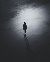 A solitary figure stands in a dimly lit, expansive space.