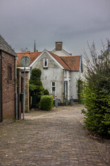 A peaceful alley with cobblestone paving, surrounded by charming houses with red-tiled roofs and lush greenery. A bike rests near a white house, creating a tranquil, village-like atmosphere.