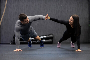 A man and woman do a synchronized high-five while holding a plank position, demonstrating teamwork...
