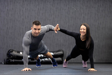 A man and woman energetically perform a synchronized high-five while holding planks in a gym,...