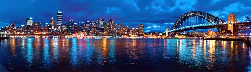Fototapeta premium Stunning Night View of Sydney Cityscape with Harbor Bridge and Reflections in Water at Dusk